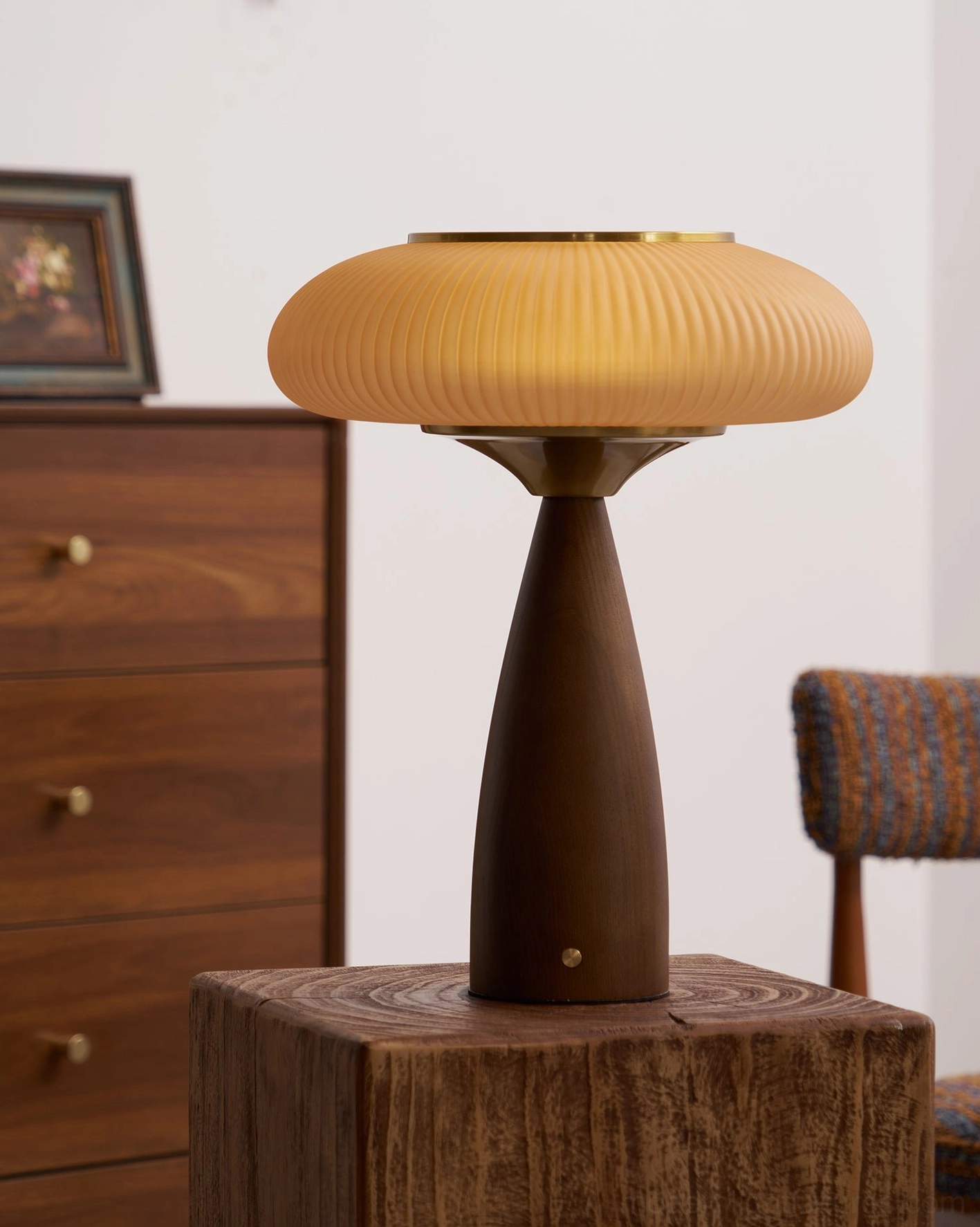 Brynn rechargeable table lamp three-quarter right side view on wood block with framed artwork and retro furniture backdrop