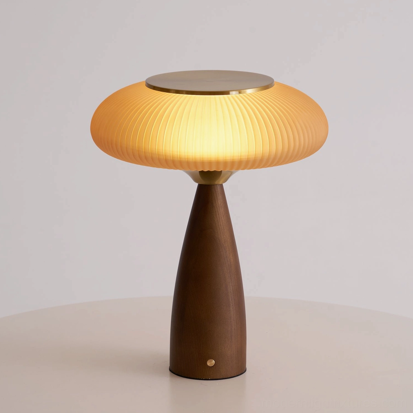 Brynn rechargeable table lamp illuminated with warm amber glow through ribbed glass shade on round side table