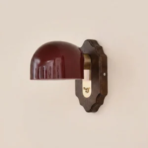 Burgundy glass dome wall sconce on beige wall, showing brass metal hardware and scalloped wood detail