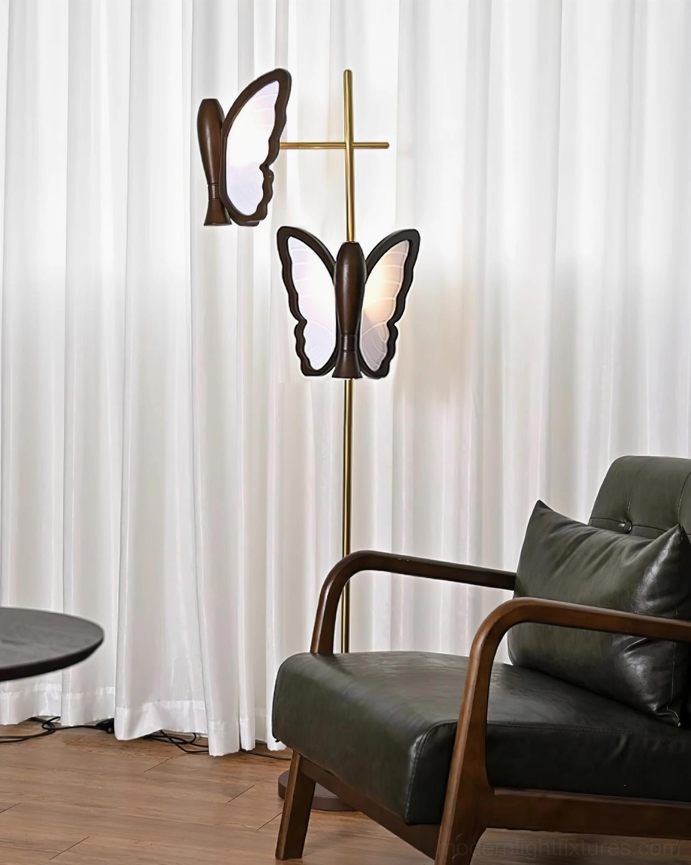 Brass gold butterfly floor lamp with dual warm-lit butterfly lamp heads, interior home setting with leather furniture
