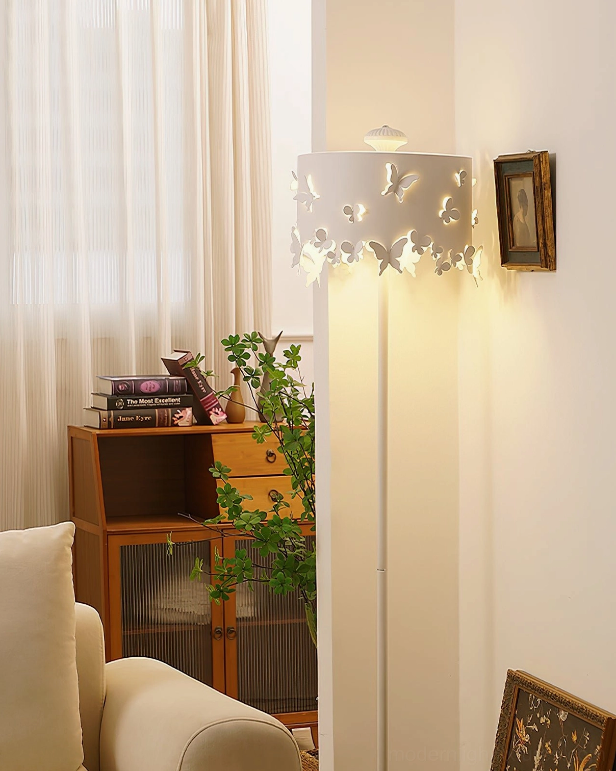 Modern butterfly floor lamp paired with wooden cabinet and green plants, creating warm aesthetic in small spaces