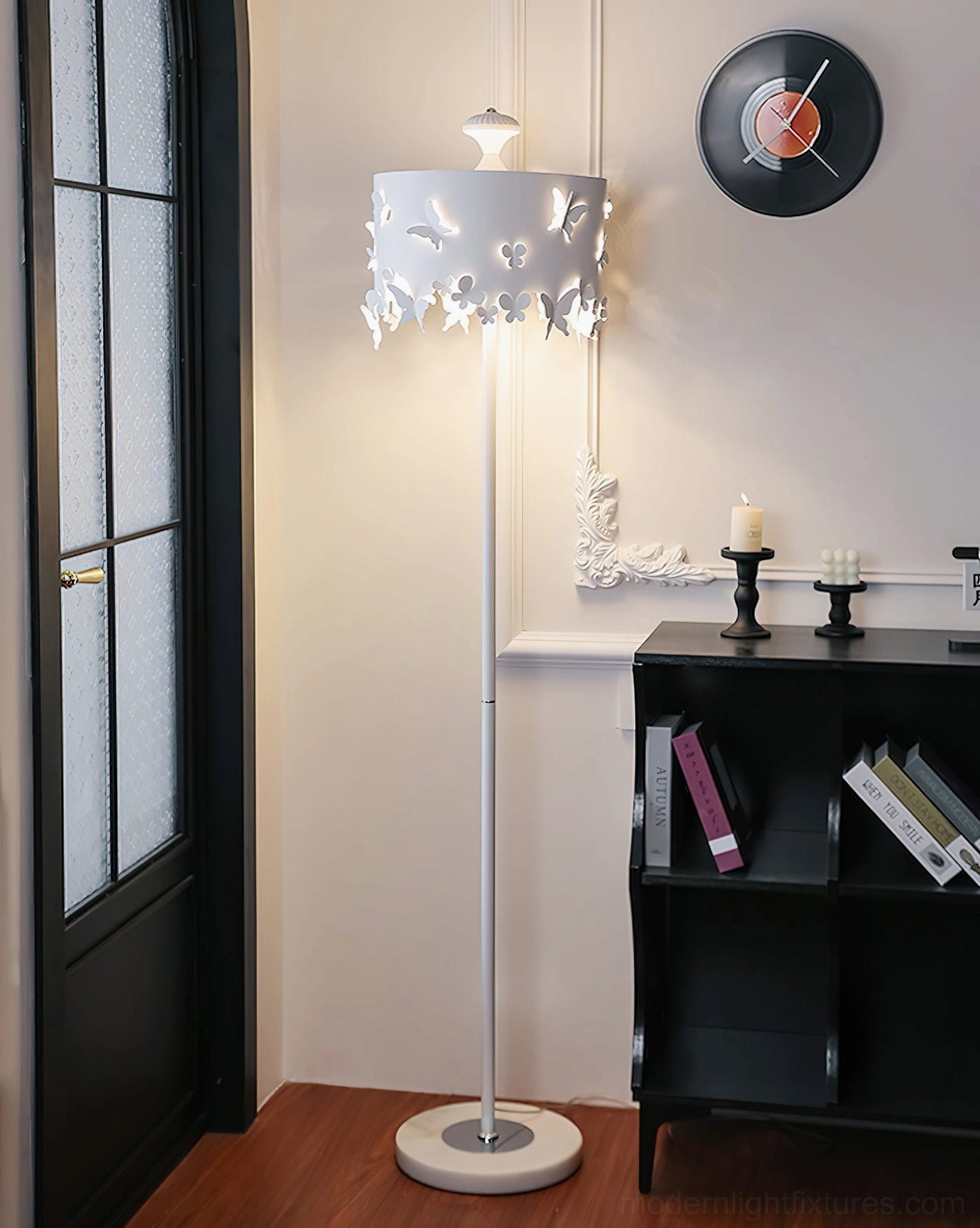 Modern butterfly floor lamp creating warm ambient lighting in vintage entryway with black shelf and vinyl wall decor, three-quarter view