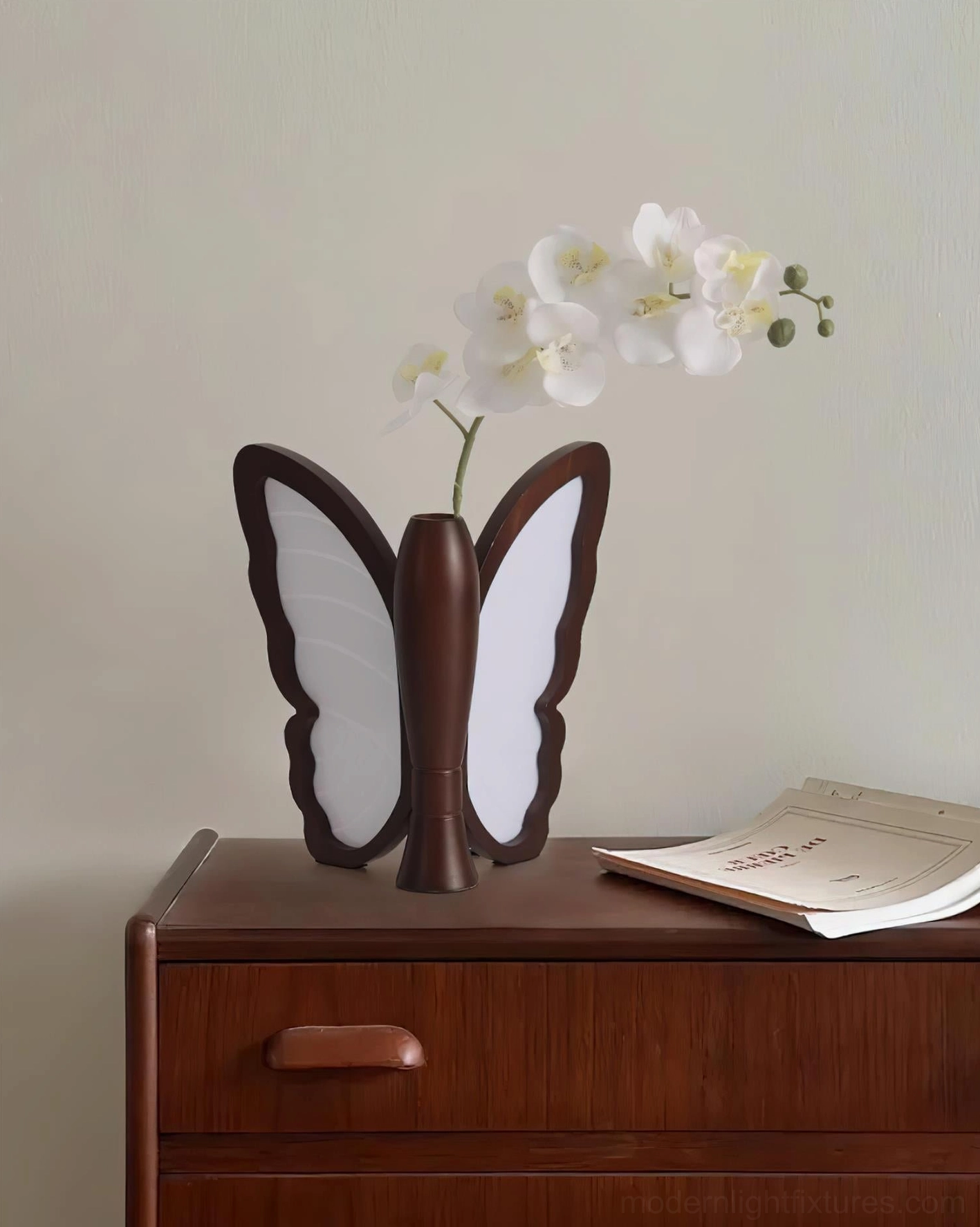 Butterfly table lamp with integrated vase holding orchid flowers on light wooden bedside dresser