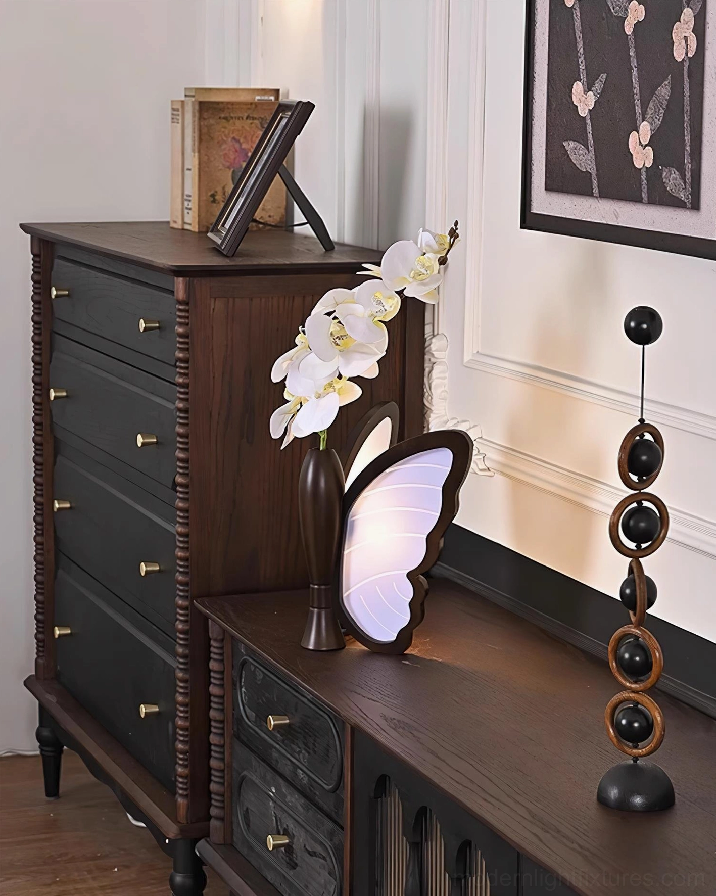 Butterfly table lamp and orchid vase arrangement on vintage wooden sideboard with decorative sculpture