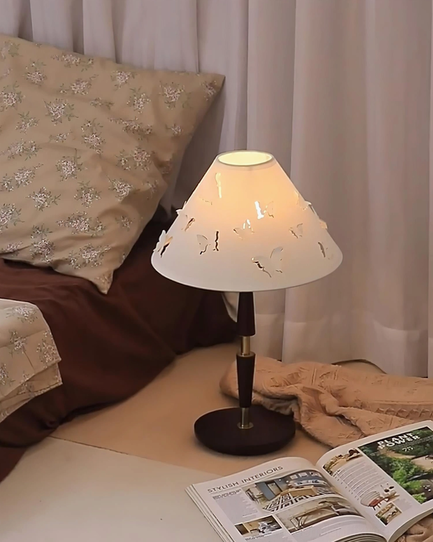 Cozy butterfly table lamp in bedroom corner with throw pillows and magazines creating intimate space