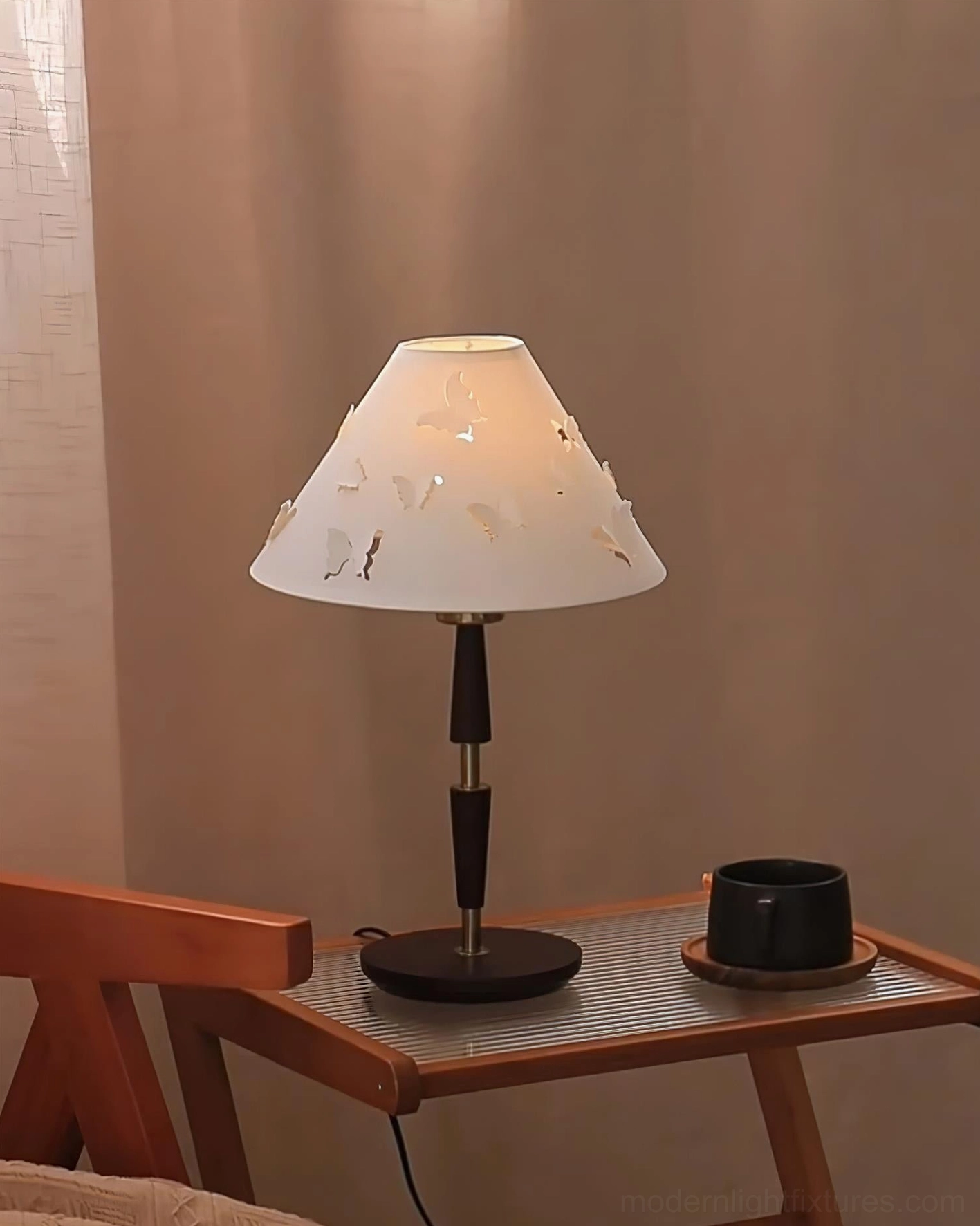 Modern butterfly perforated lamp on wooden side table beside black ceramic mug home decor
