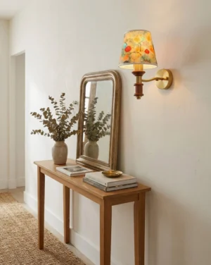 Calantha brass wall sconce with floral shade installed above wooden console table in entryway corner, warm neutral interior design