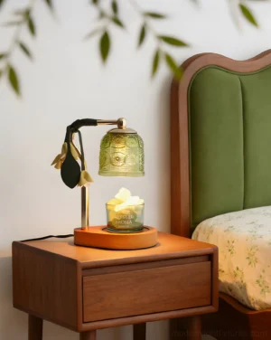 Decorative candle warmer lamp displayed on bedroom nightstand with green upholstered headboard, creating cozy ambient lighting