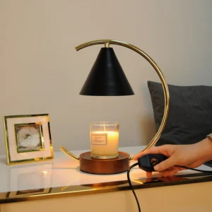 Candle warmer lamp on bedroom vanity table with person adjusting power switch, scented candle lit, warm ambient lighting with decorative frames