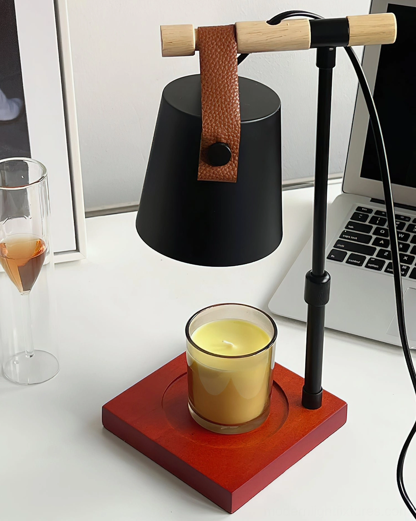 Black metal candle warmer lamp with red wooden base displayed on home office desk with laptop and wine glass