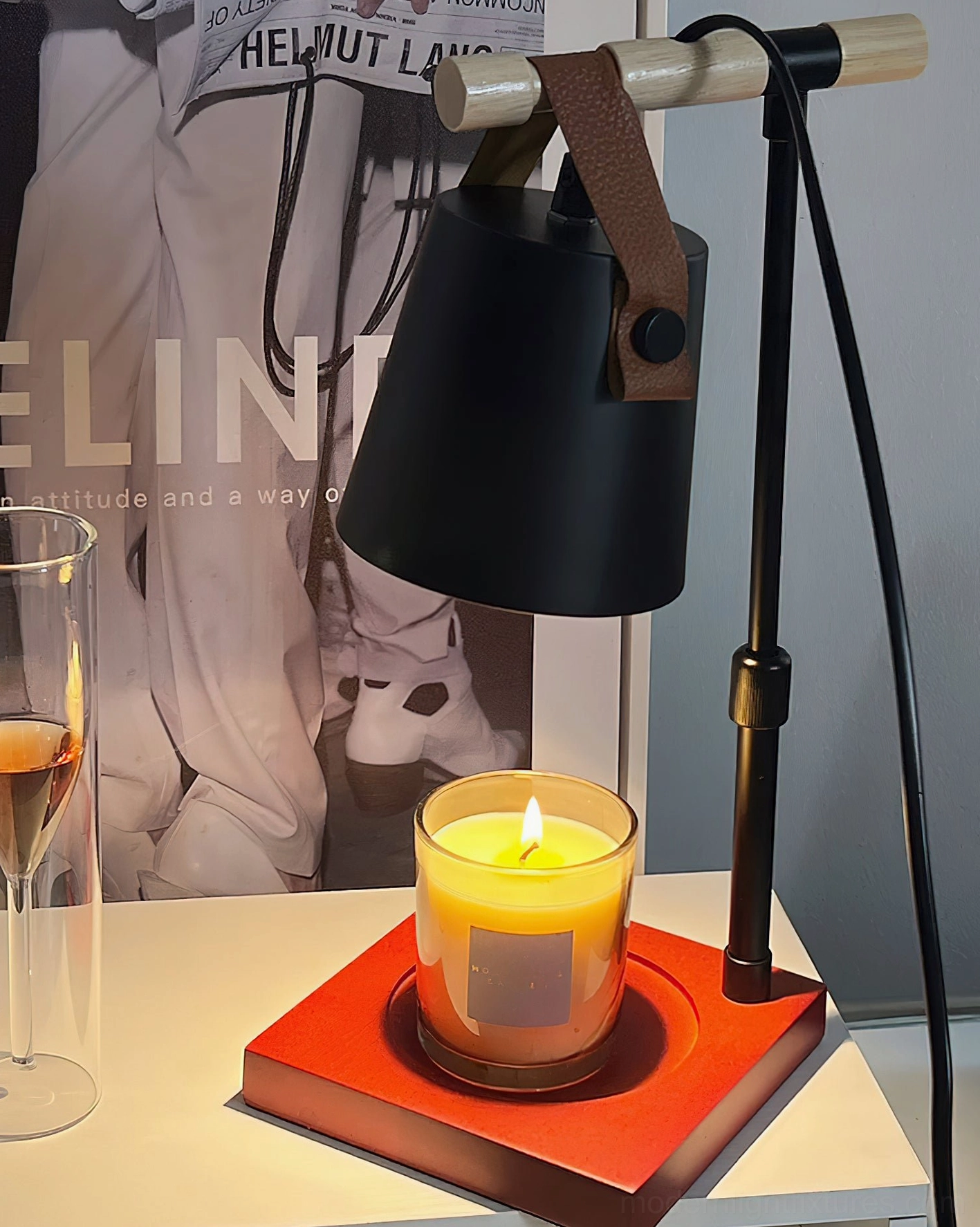Black candle warmer lamp with red wood base and lit scented candle on home office desk with fashion poster backdrop