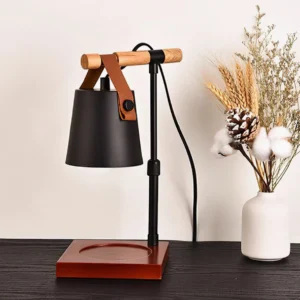 Black candle warmer lamp with wooden base styled on dark wood table with dried flowers and white ceramic vase, three-quarter view