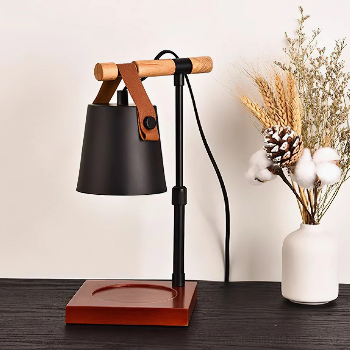 Black candle warmer lamp with wooden base styled on dark wood table with dried flowers and white ceramic vase, three-quarter view