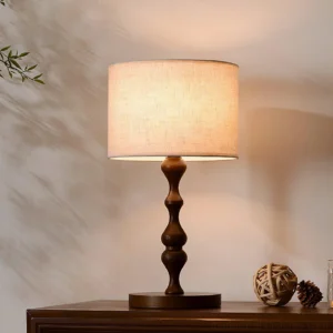 Wooden table lamp with carved ash wood pedestal base and textured linen shade on side table