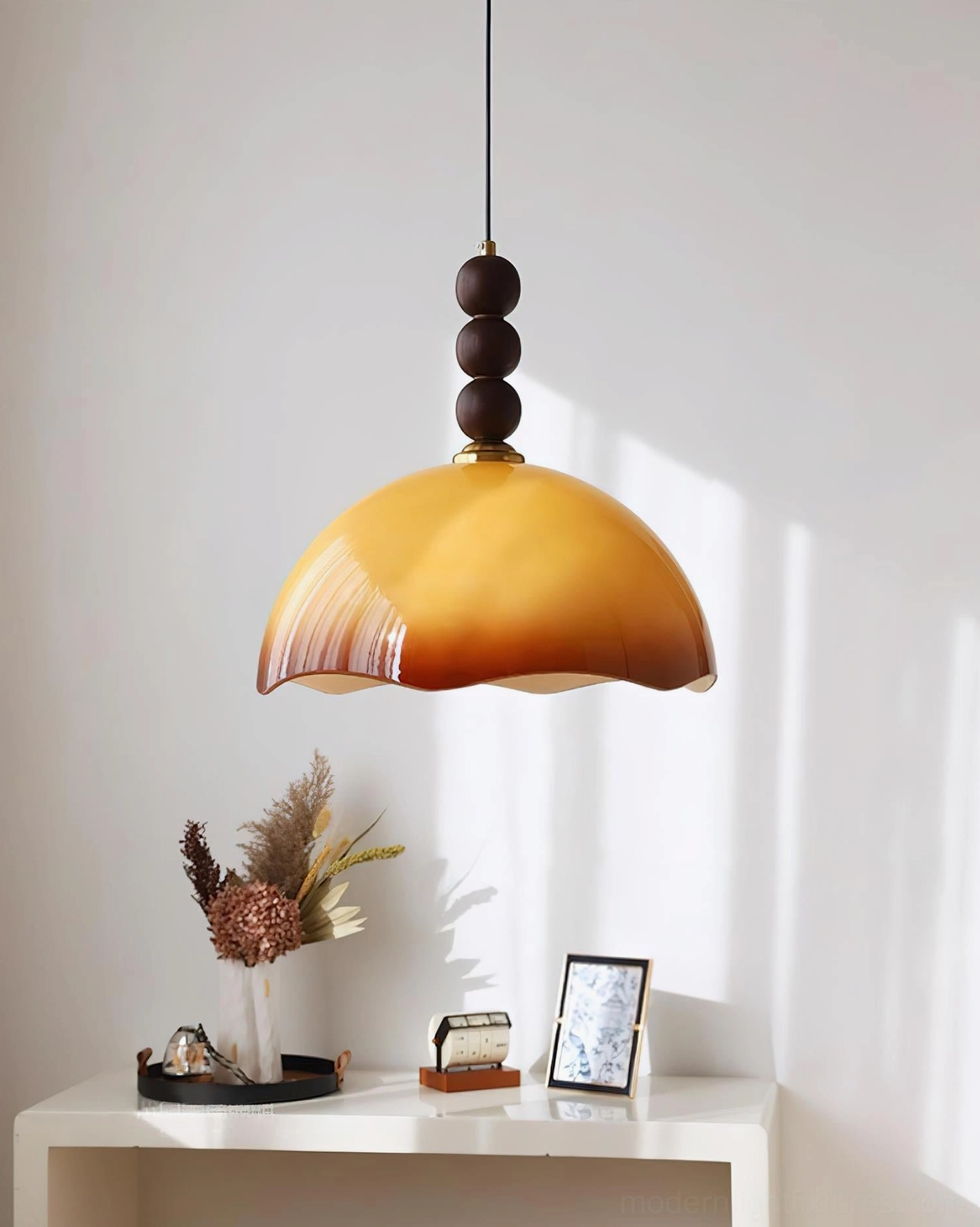 Front three-quarter hanging view of caramel glass pendant light with brass hardware and walnut wood sphere in sunlit interior