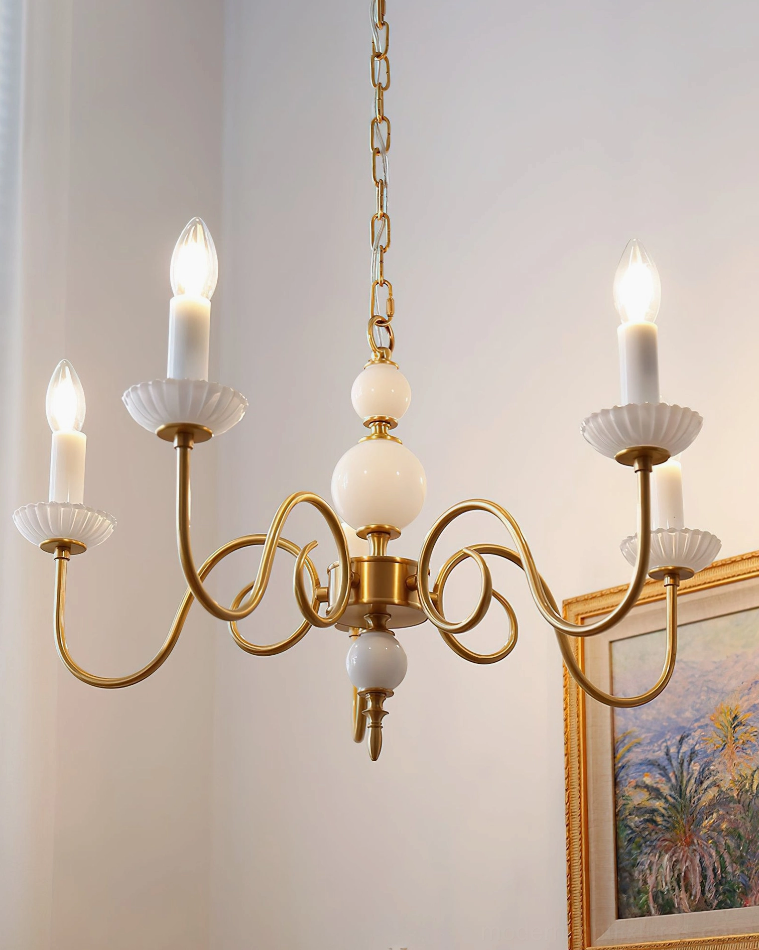 Lit brass candle chandelier with illuminated bulbs in residential room with framed artwork