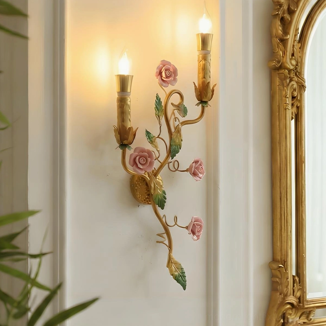 Pink rose variant of Carmelia wall sconce displayed above vintage gold mirror in elegant interior setting