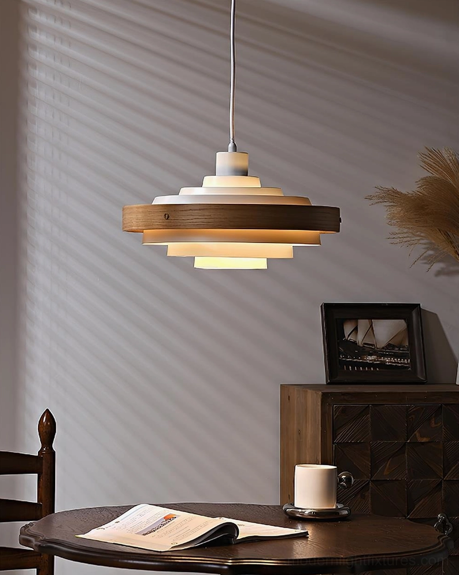 Carmen tiered pendant light above round wooden dining table in modern minimalist dining corner with framed artwork and dried plants