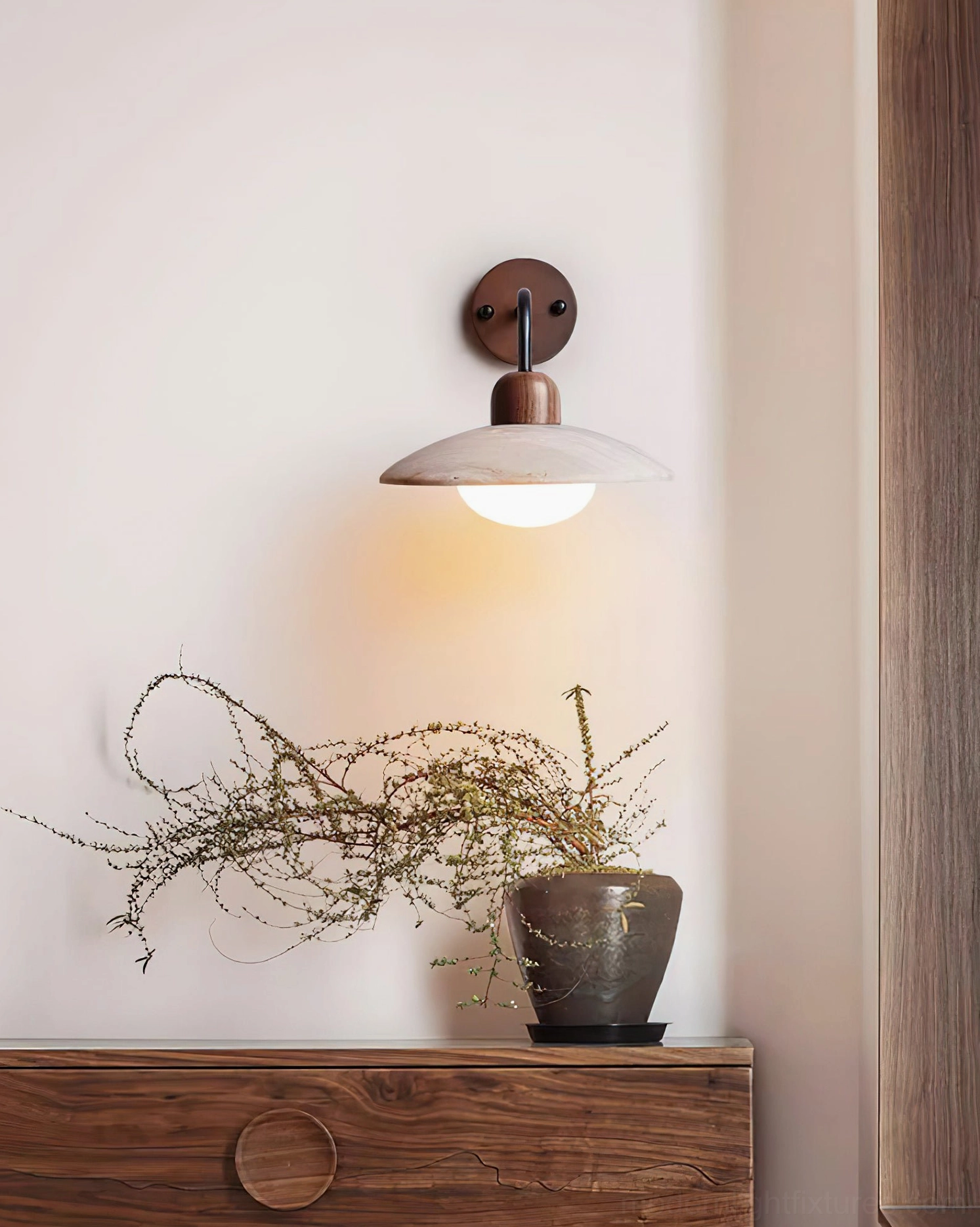 Compact travertine wall sconce with dark wood base and saucer shade positioned above console table entryway