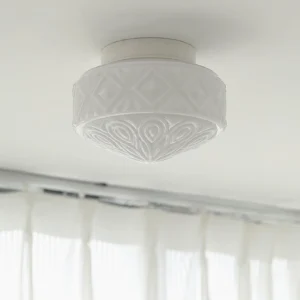Vintage glass flush mount ceiling light installed on home ceiling, low-angle view showing carved texture and warm illumination