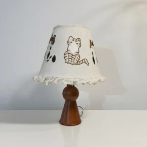 Whimsical cat-themed table lamp three-quarter view showing ruffled edge and warm wooden stem
