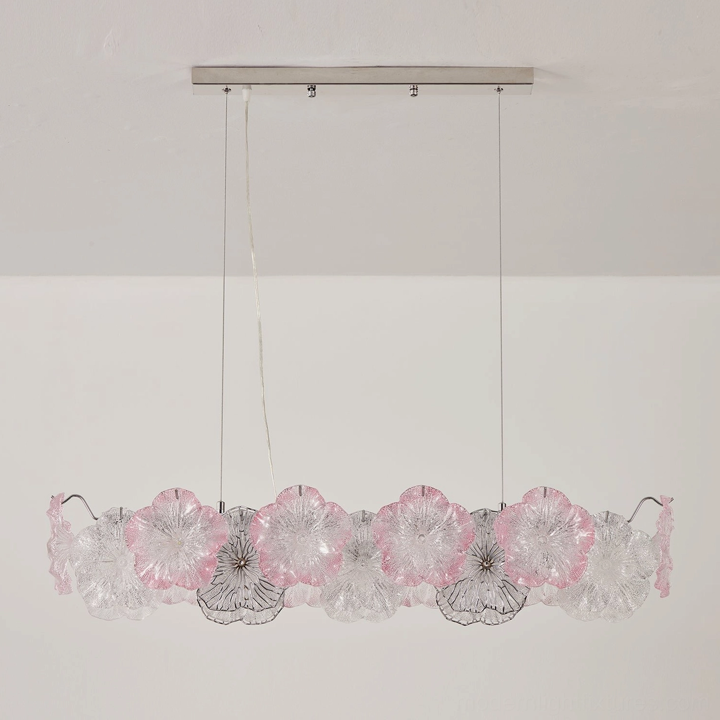 Celadine linear chandelier with blush pink tinted glass petals mixed with clear over dining table, warm interior lighting