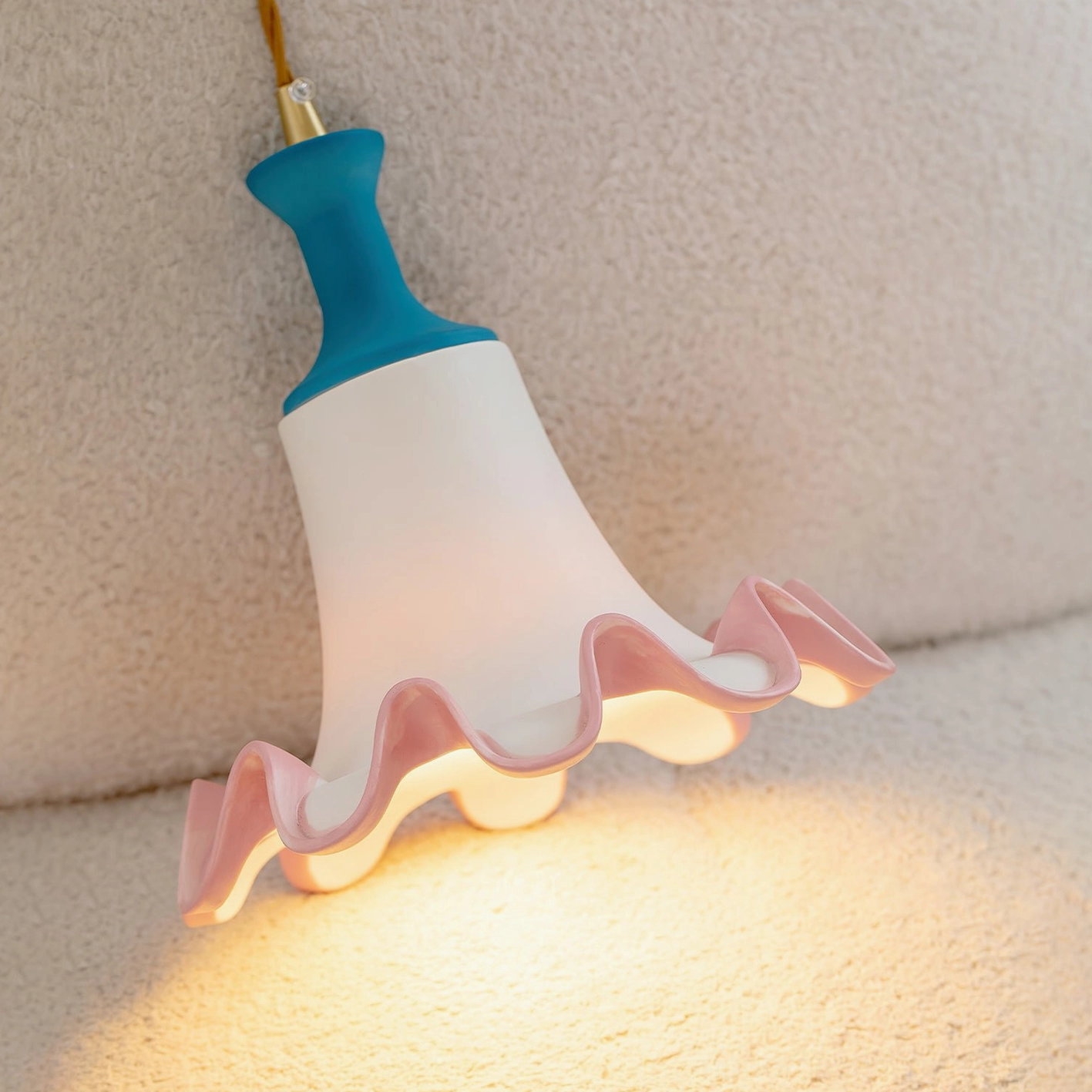 Celina ceramic pendant light low side angle view showing warm interior glow and textured plush backdrop environment