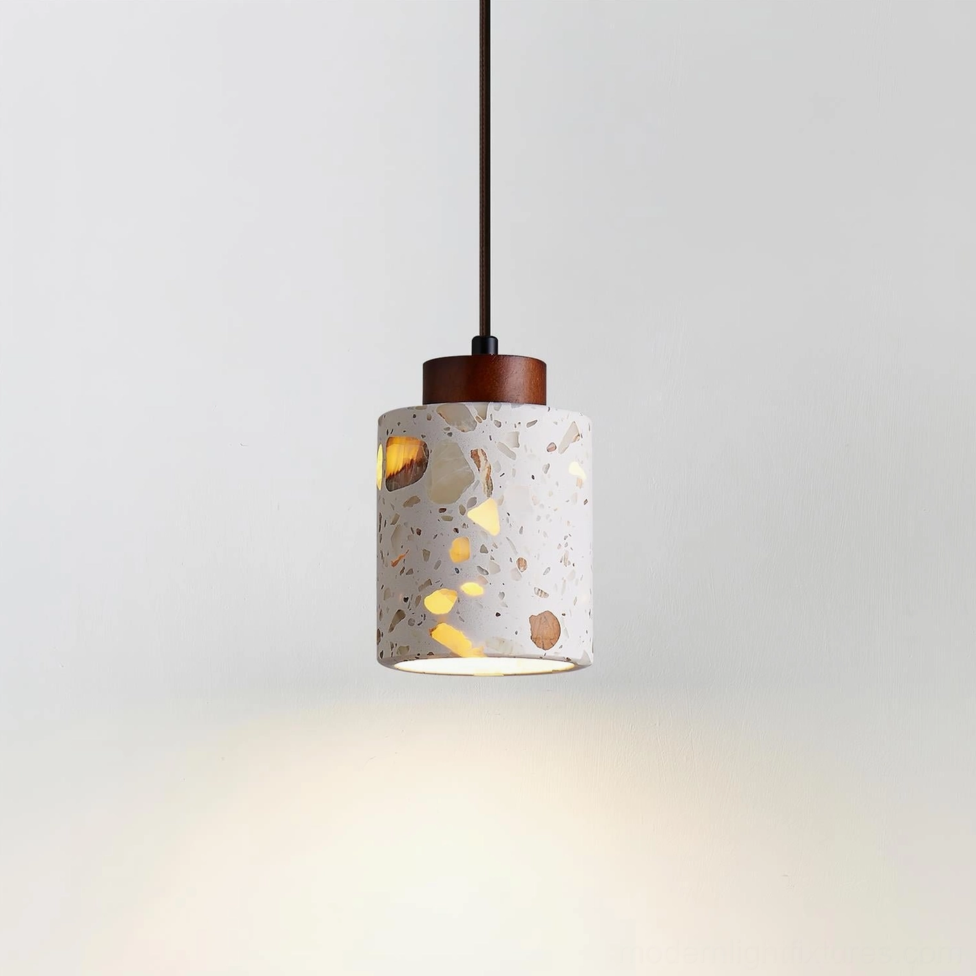 Illuminated cemento pendant lamp emitting warm ambient light through textured terrazzo material