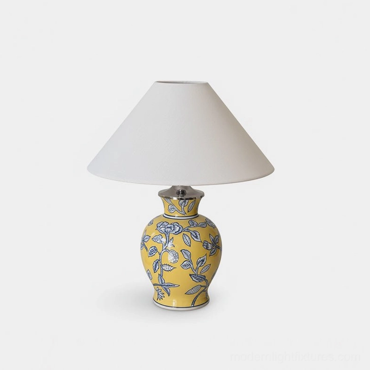 Ceramic floral table lamp with yellow base and blue botanical pattern, fabric shade on white studio background