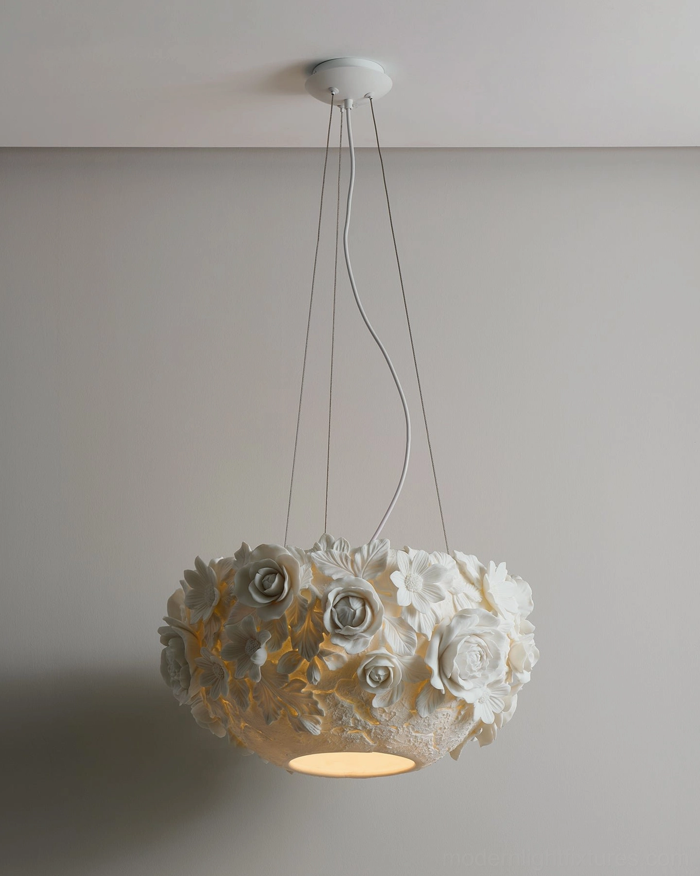 Front low-angle view of illuminated ceramic flower bouquet pendant lamp with exposed suspension wires against neutral wall