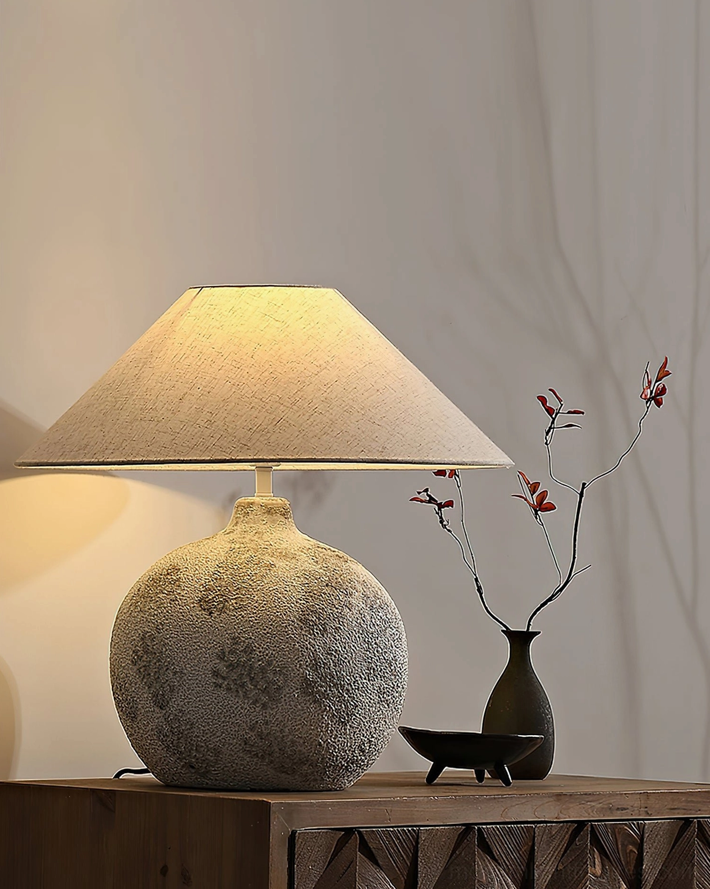 Ceramic table lamp with black vase and decorative tray on side table in contemporary interior setting with textured ambient lighting