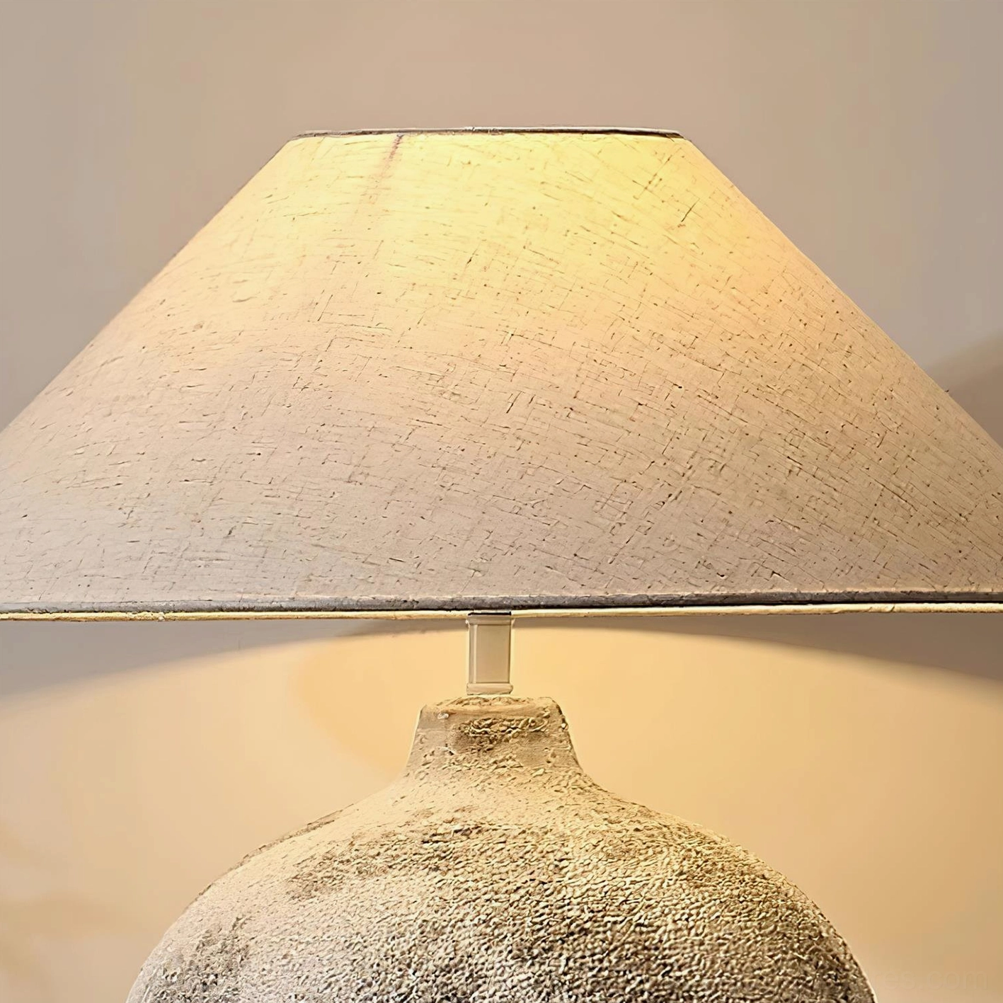 Close-up detail shot of ceramic table lamp showing rough textured ceramic base and linen fabric shade with warm light diffusion