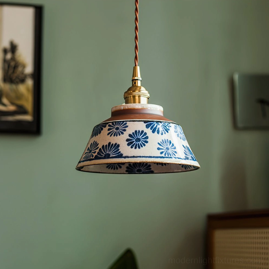 Ceramic pendant light with hand-painted blue daisy pattern and brass hardware mounted against green wall