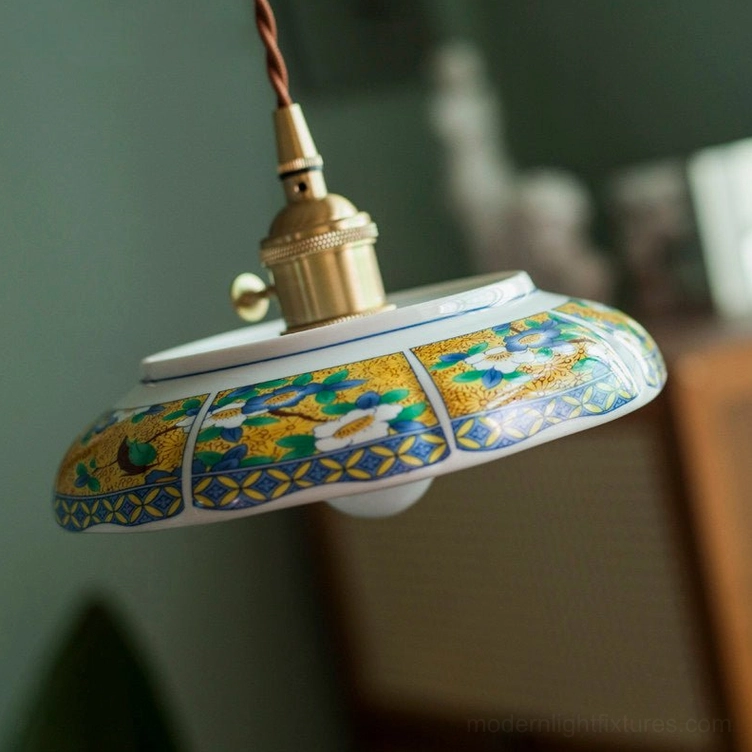 Close-up detail of hand-painted ceramic shade with floral or landscape pattern, brass socket, and twisted fabric cord