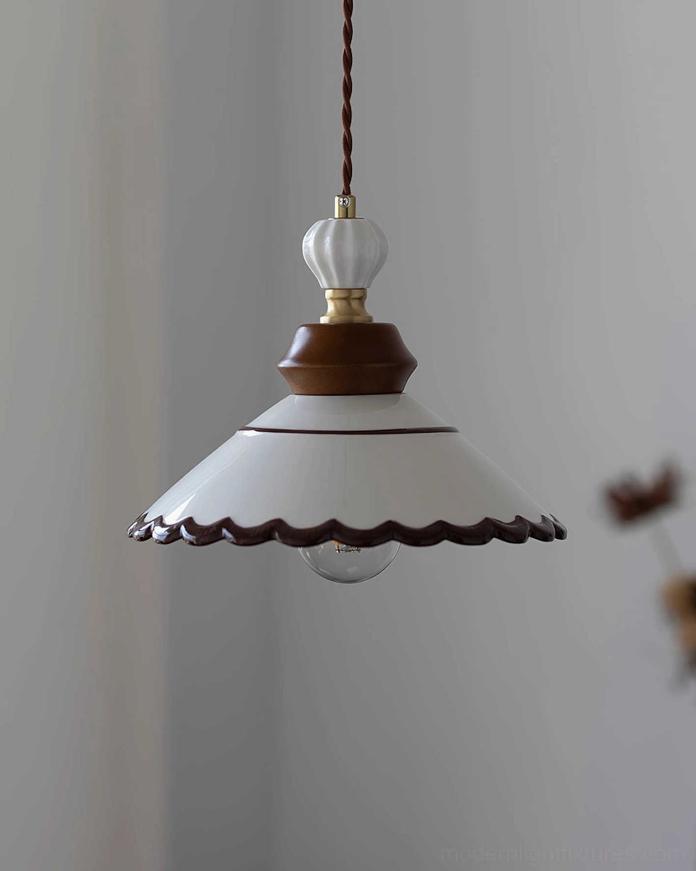 Ceramic pendant light with twisted fabric cord and brass accents, showing vintage design elements in home setting