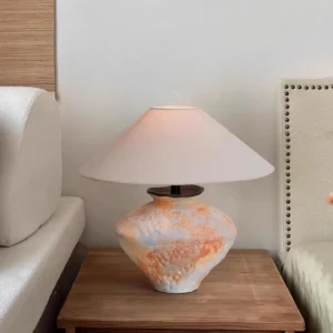 Handcrafted ceramic lamp displayed on bedroom nightstand beside upholstered furniture with warm ambient lighting
