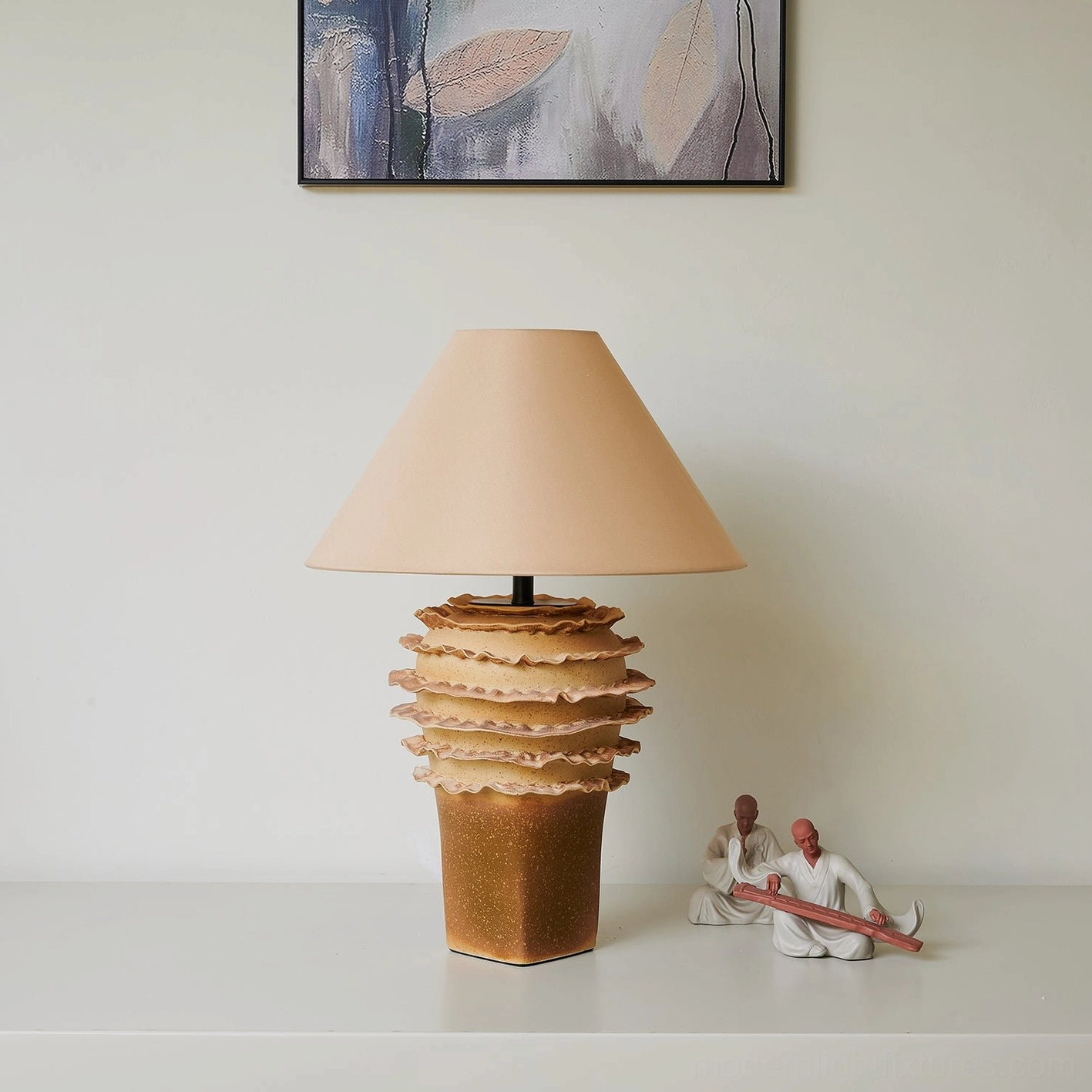 Beige ceramic layered table lamp with fabric shade on display with wall art and decorative objects