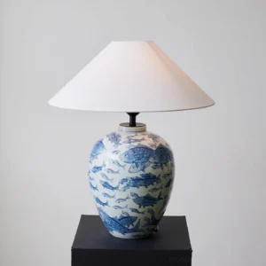 Hand-painted blue and white ceramic table lamp displayed on black square pedestal, three-quarter angled perspective
