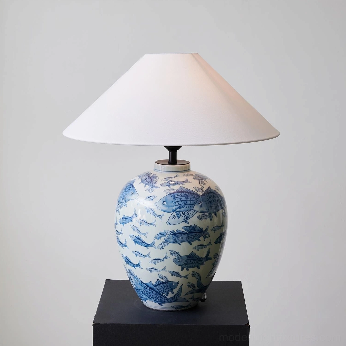 Hand-painted blue and white ceramic table lamp displayed on black square pedestal, three-quarter angled perspective