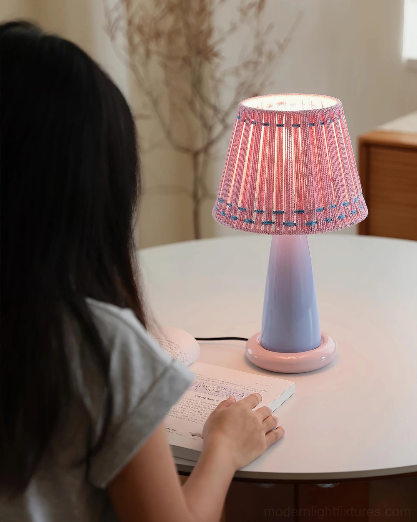 Lit ceramic table lamp in home study room with person working, pink woven shade providing soft focused lighting
