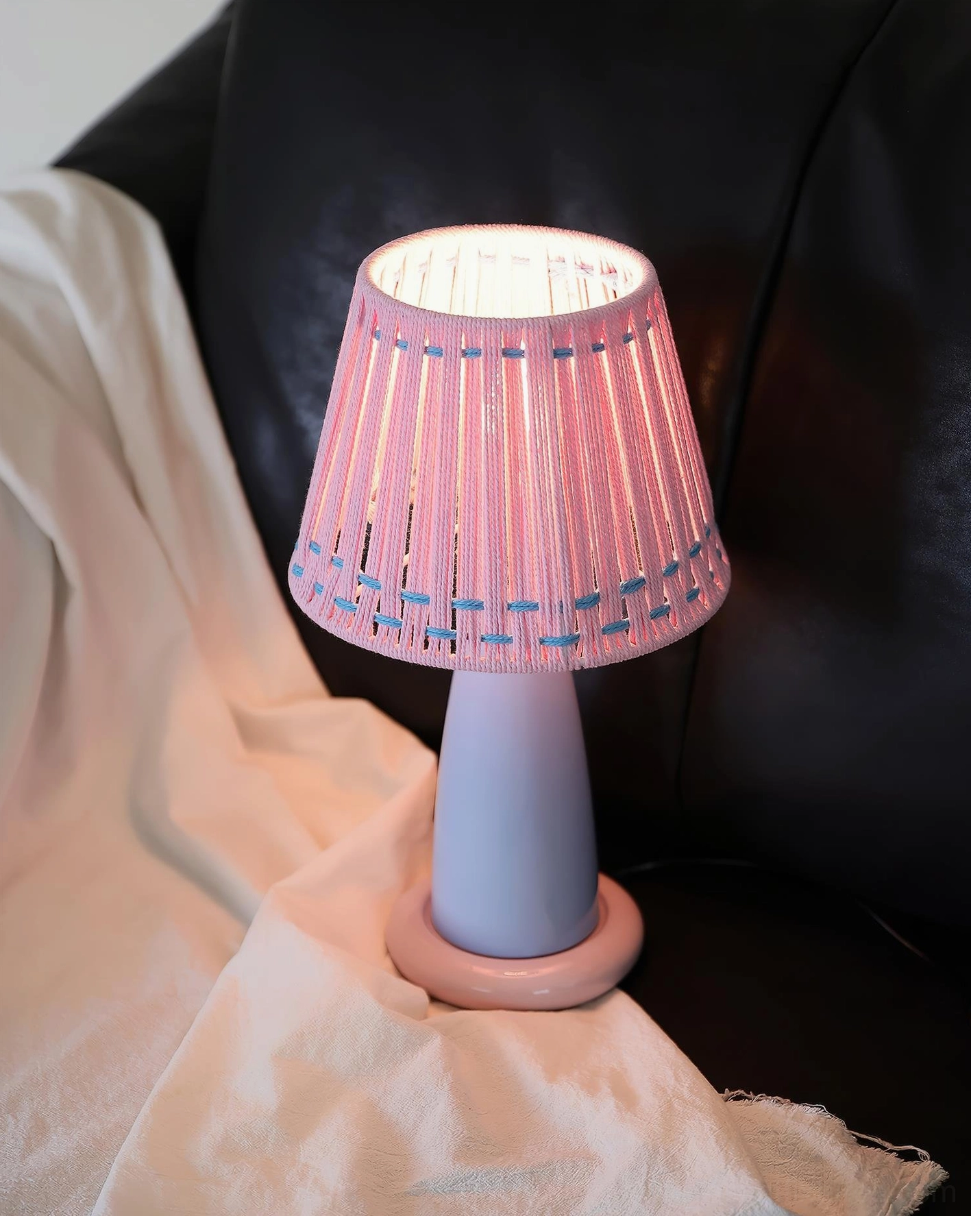 Illuminated ceramic table lamp with pink woven shade and blue ceramic base, providing warm ambient lighting on leather sofa setting