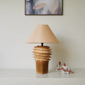 Modern ceramic layered table lamp in neutral tones displayed on tabletop with decorative figurines