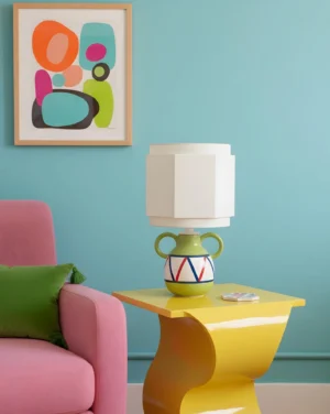 Three-quarter angle view of geometric table lamp displayed on modern yellow side table in contemporary living room setting with pink chair