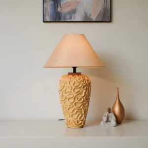 Sculptural ceramic table lamp with intricate carved details displayed with decorative accessories in warm neutral styling