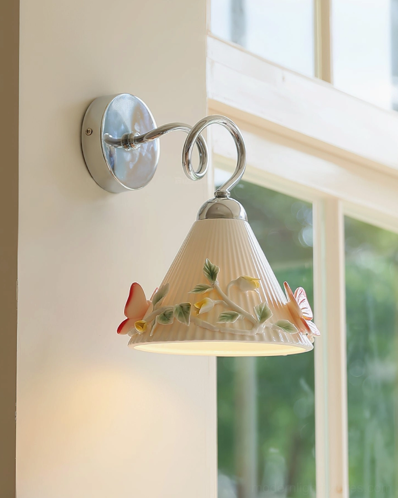 Florynna ceramic butterfly wall sconce three-quarter side view showing polished chrome bracket, ribbed beige shade with botanical embellishments and sculptural details