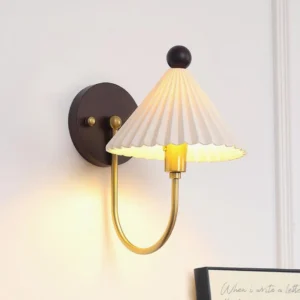 White pleated ceramic wall sconce illuminated showing warm ambient glow with brass hardware details and decorative frame styling