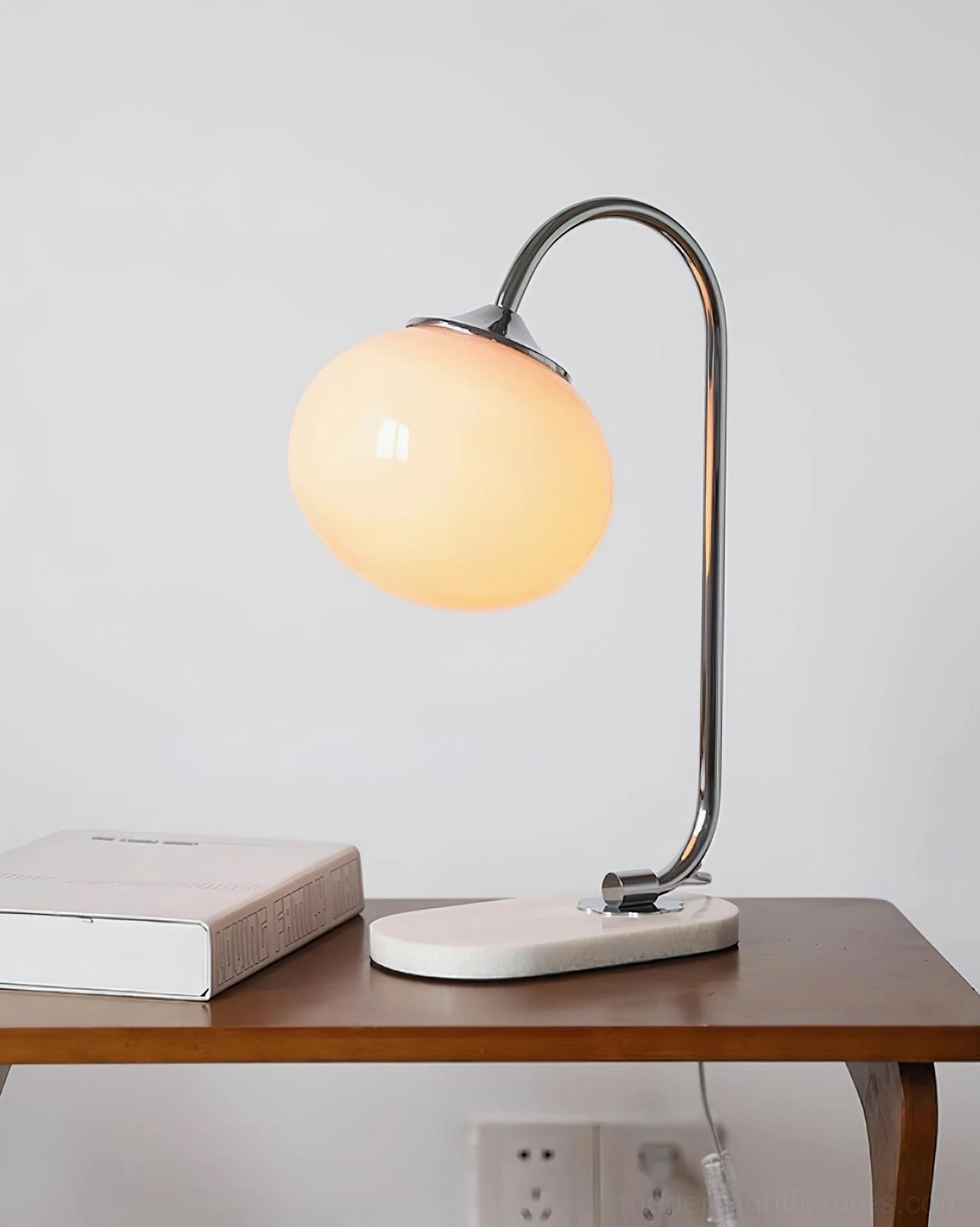 Chrome silver globe table lamp with lit warm amber glass shade, marble base, and books styling