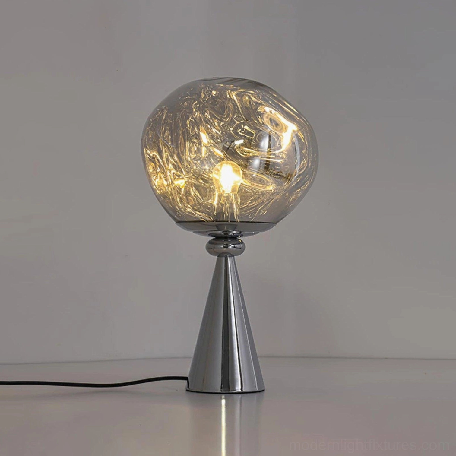 Chrome molten glass cone lamp flat perspective tabletop display with power cord visible warm light