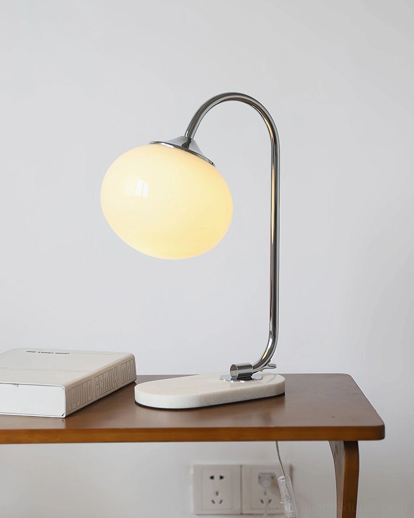 Chrome silver metal globe table lamp with white marble base and clear glass shade on side table with books
