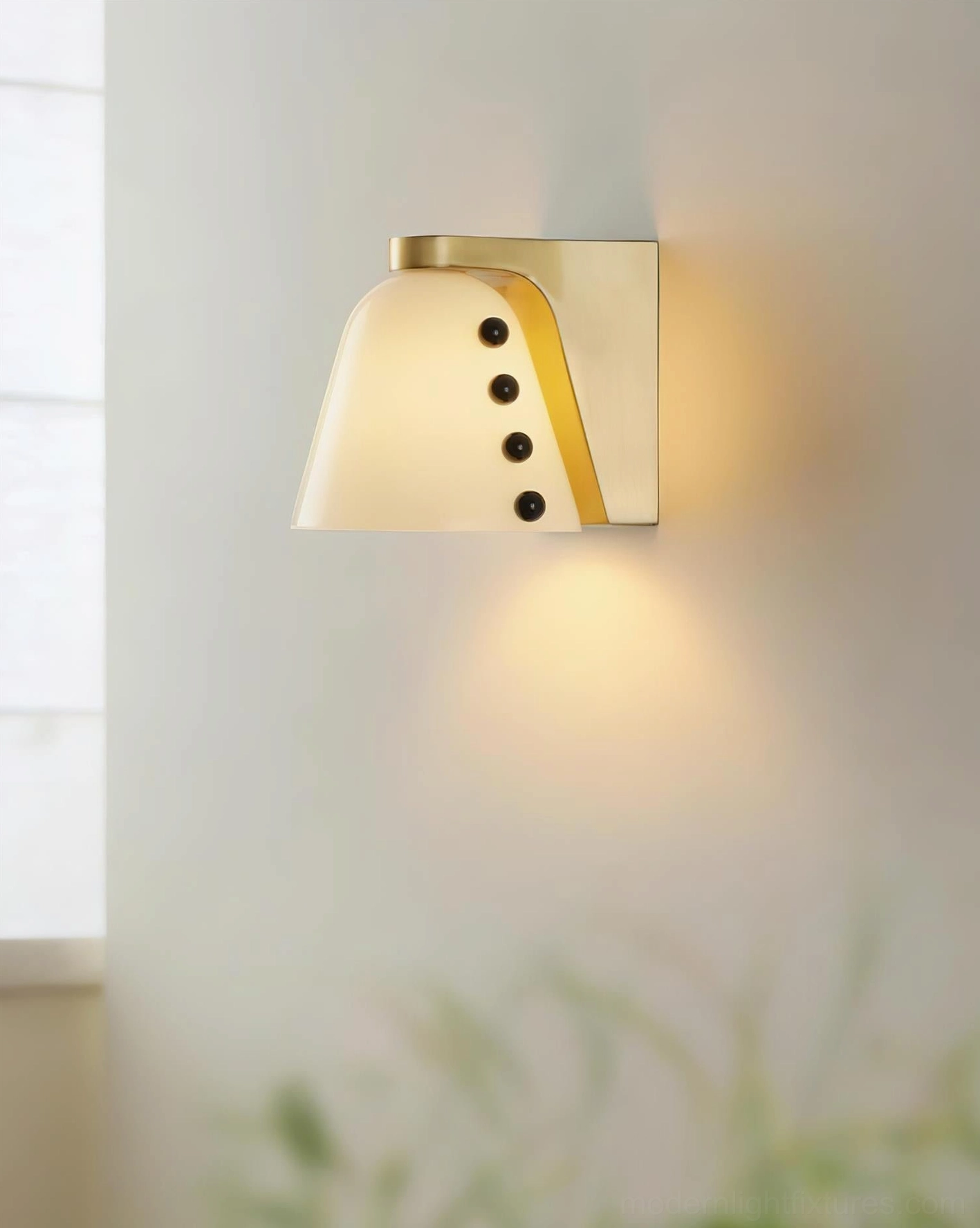Modern wall sconce with beige conical glass shade mounted on brass fixture with black spherical details in cozy home interior setting